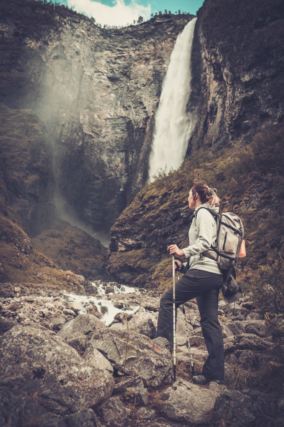 Woman hiker with backpack standing near Vettisfossen waterfall.