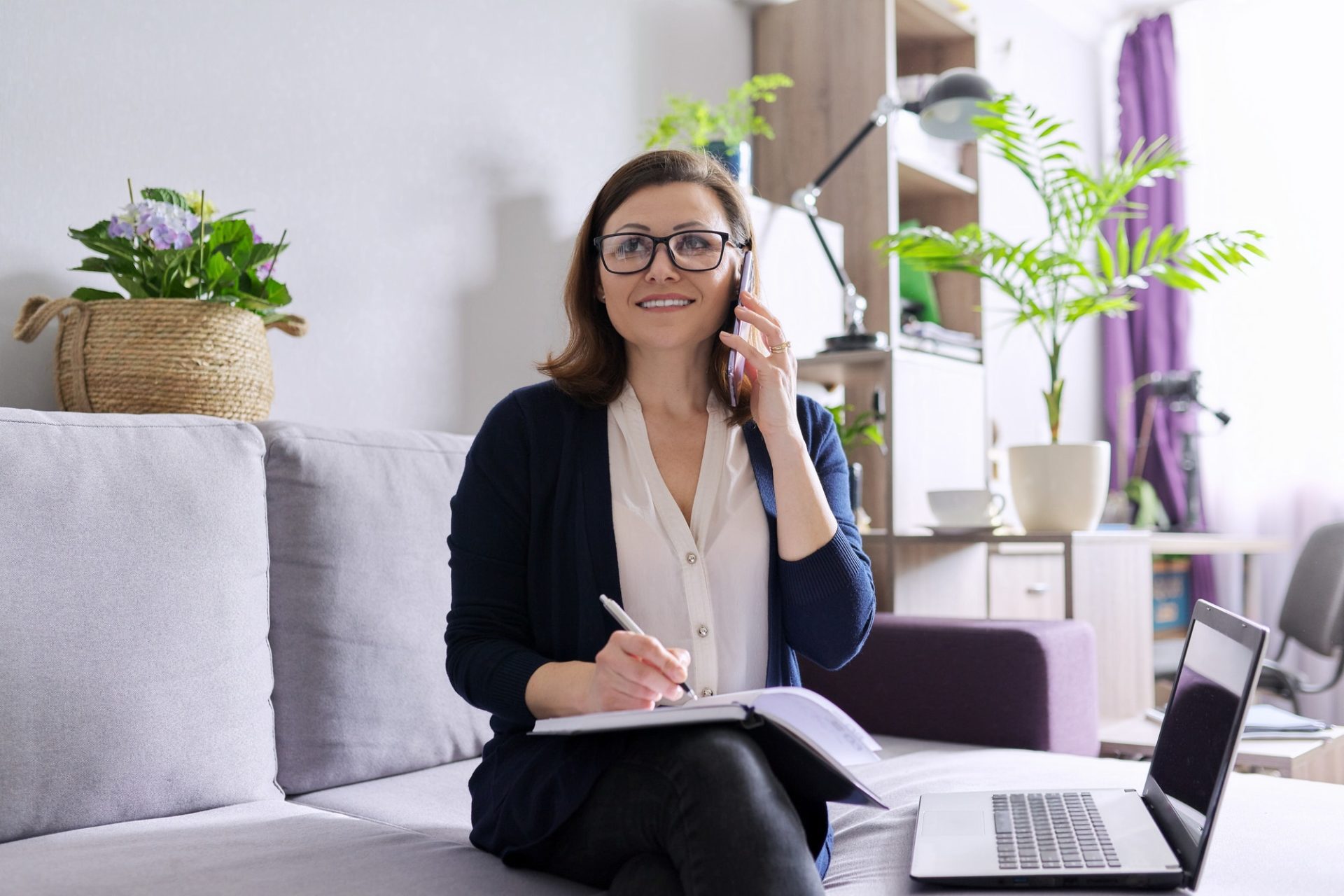 Business female freelancer sitting on sofa with laptop, talking on phone