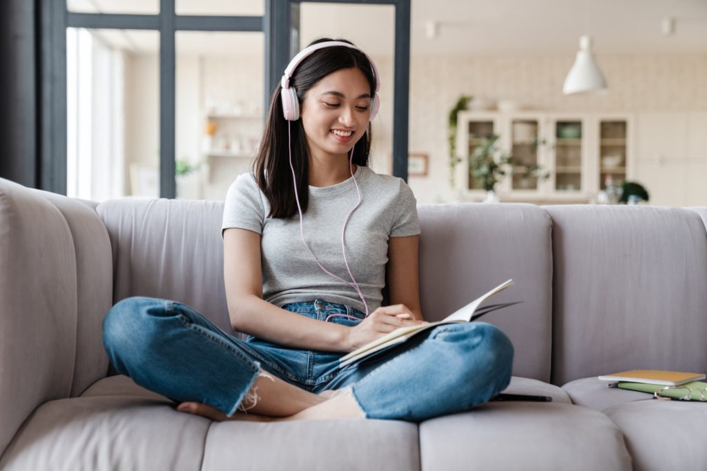 Image of happy asian woman using headphones and writing down notes