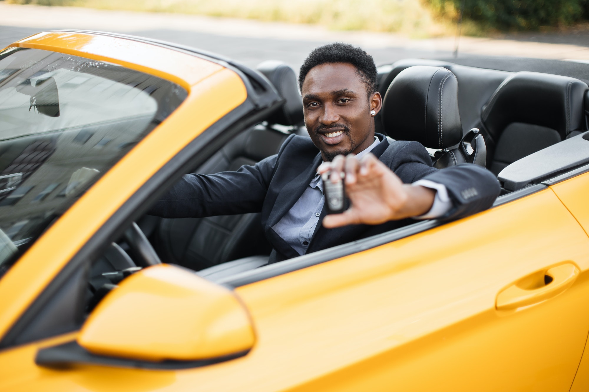 African american businessman in suit sitting inside his luxury sport car with keys in hands.