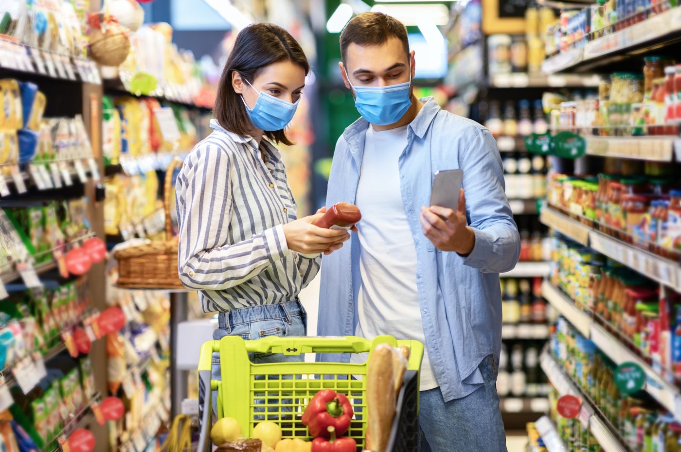 Young family in masks with phone shopping in supermarket
