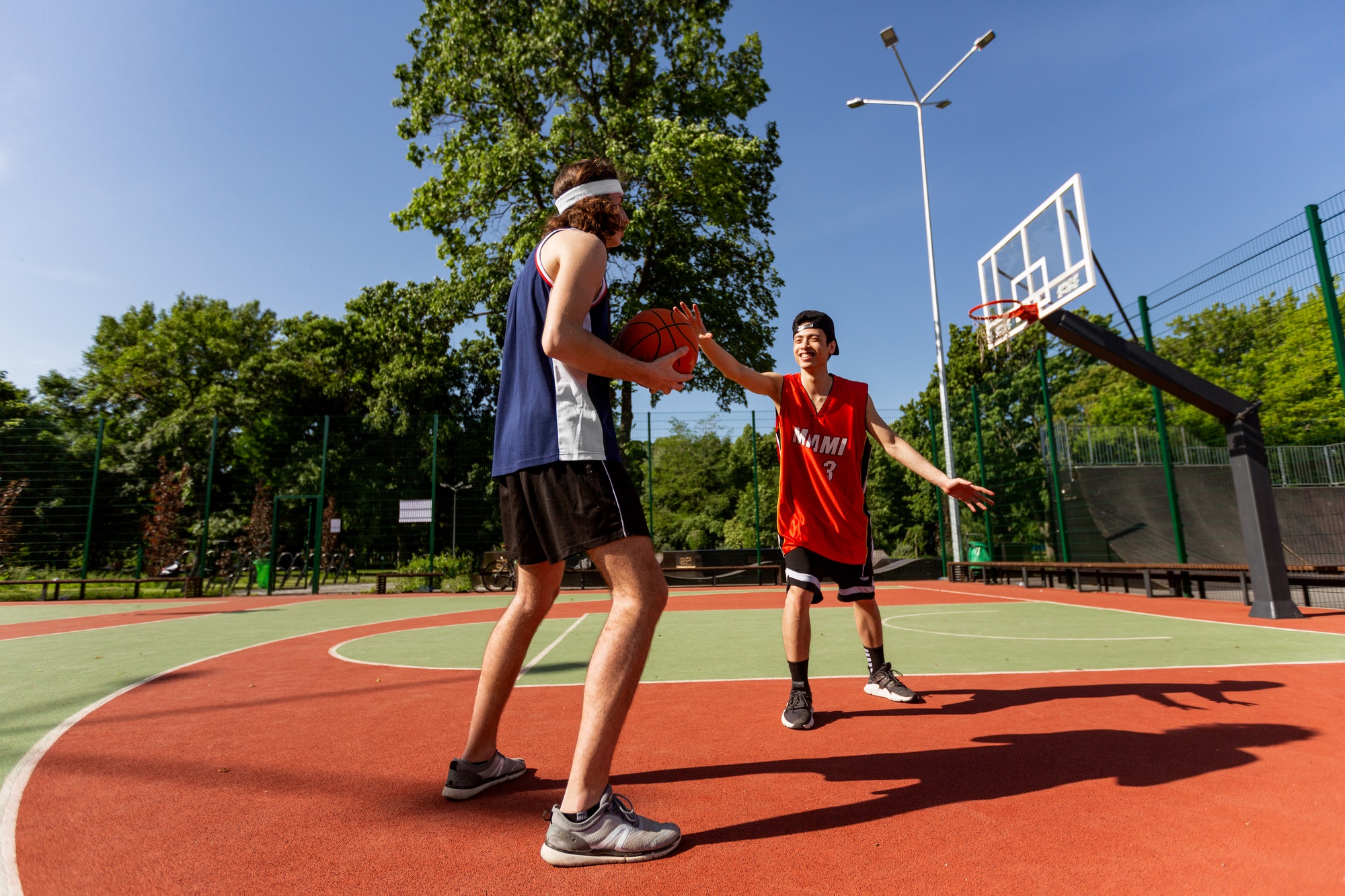 Two millennial sportsmen playing basketball match at outdoor playground, blank space