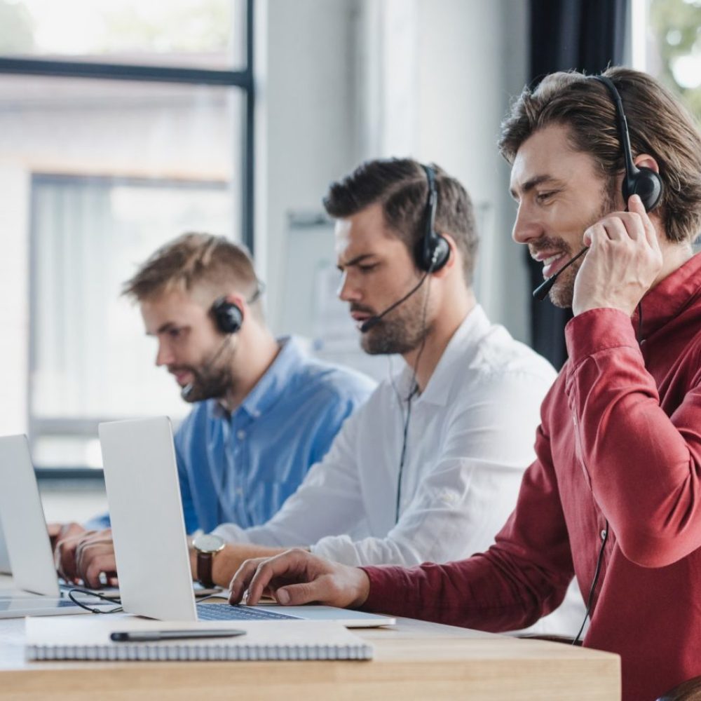 three young call center operators in headsets using laptops in office