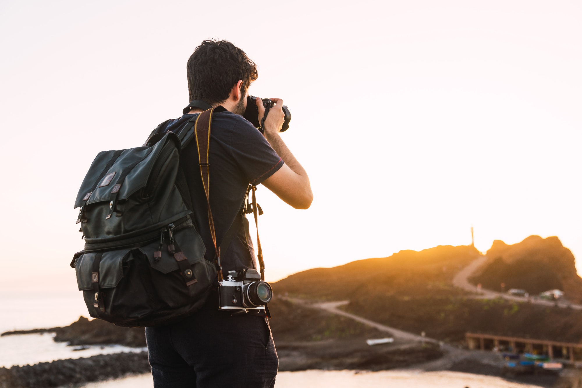 Person with vintage camera and backpack on mountain at sunset