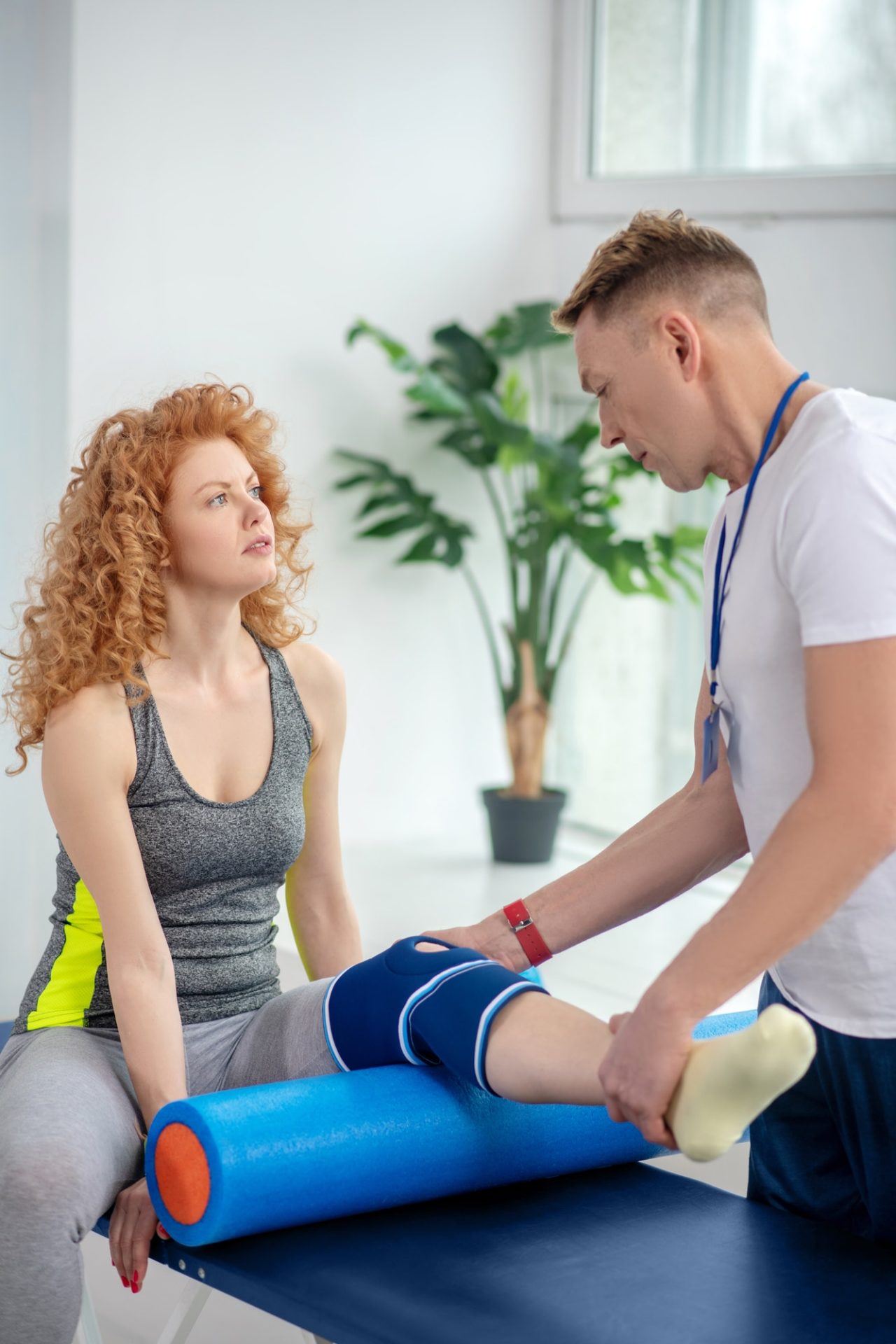 Male physiotherapist examining knee bandage of female patient sitting with knee bolster