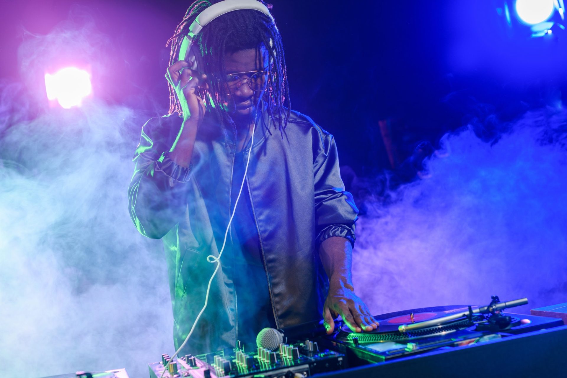professional african american club DJ in headphones with sound mixer in nightclub