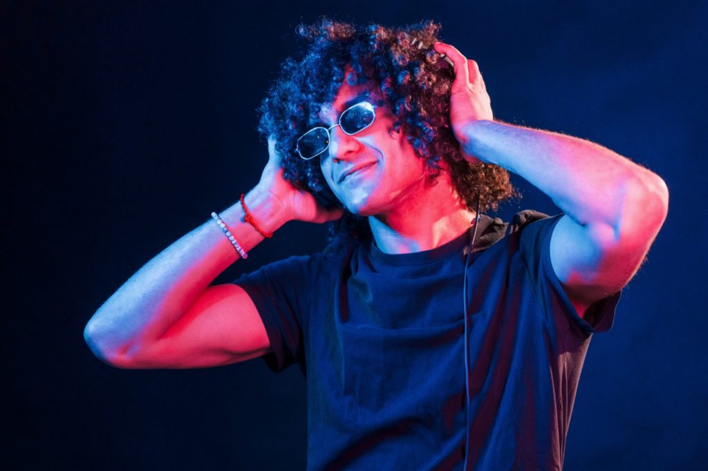 Young DJ with curly hair standing in the club with neon light