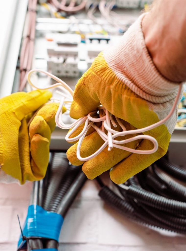 Cropped view of electrician in gloves holding wires near electrical box