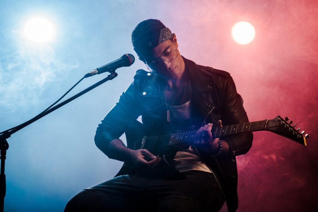 focused male musician playing on electric guitar near microphone on stage during rock concert