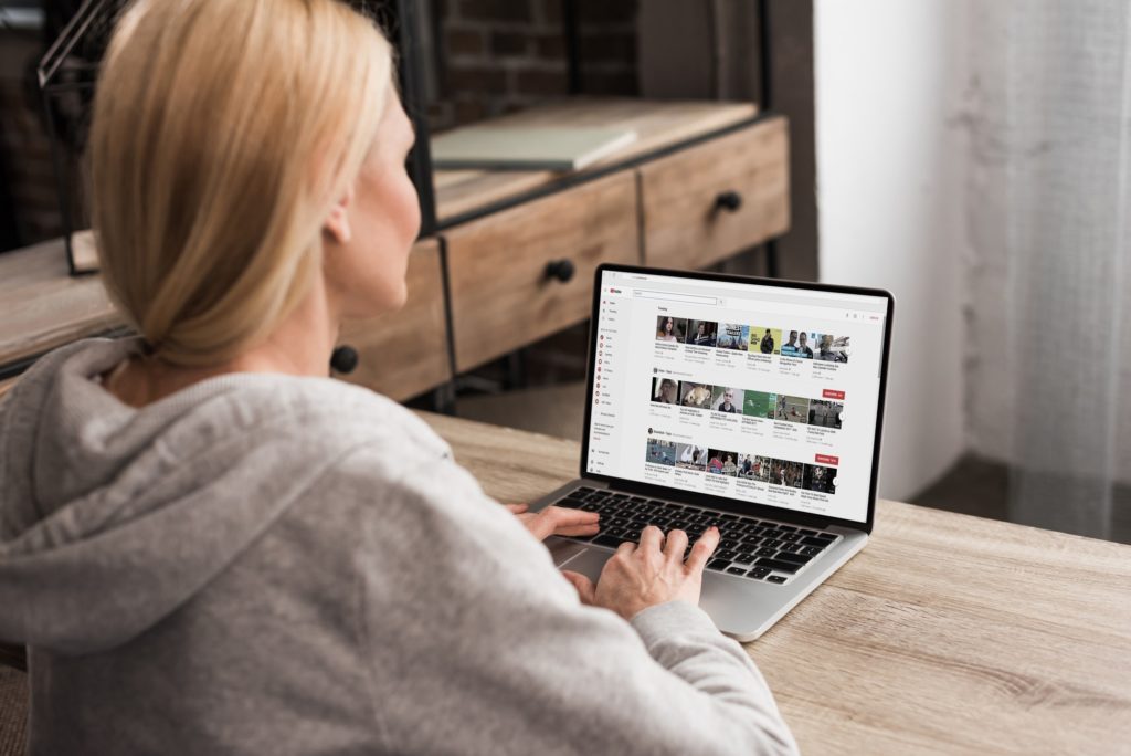 back view of woman using laptop with youtube website on screen