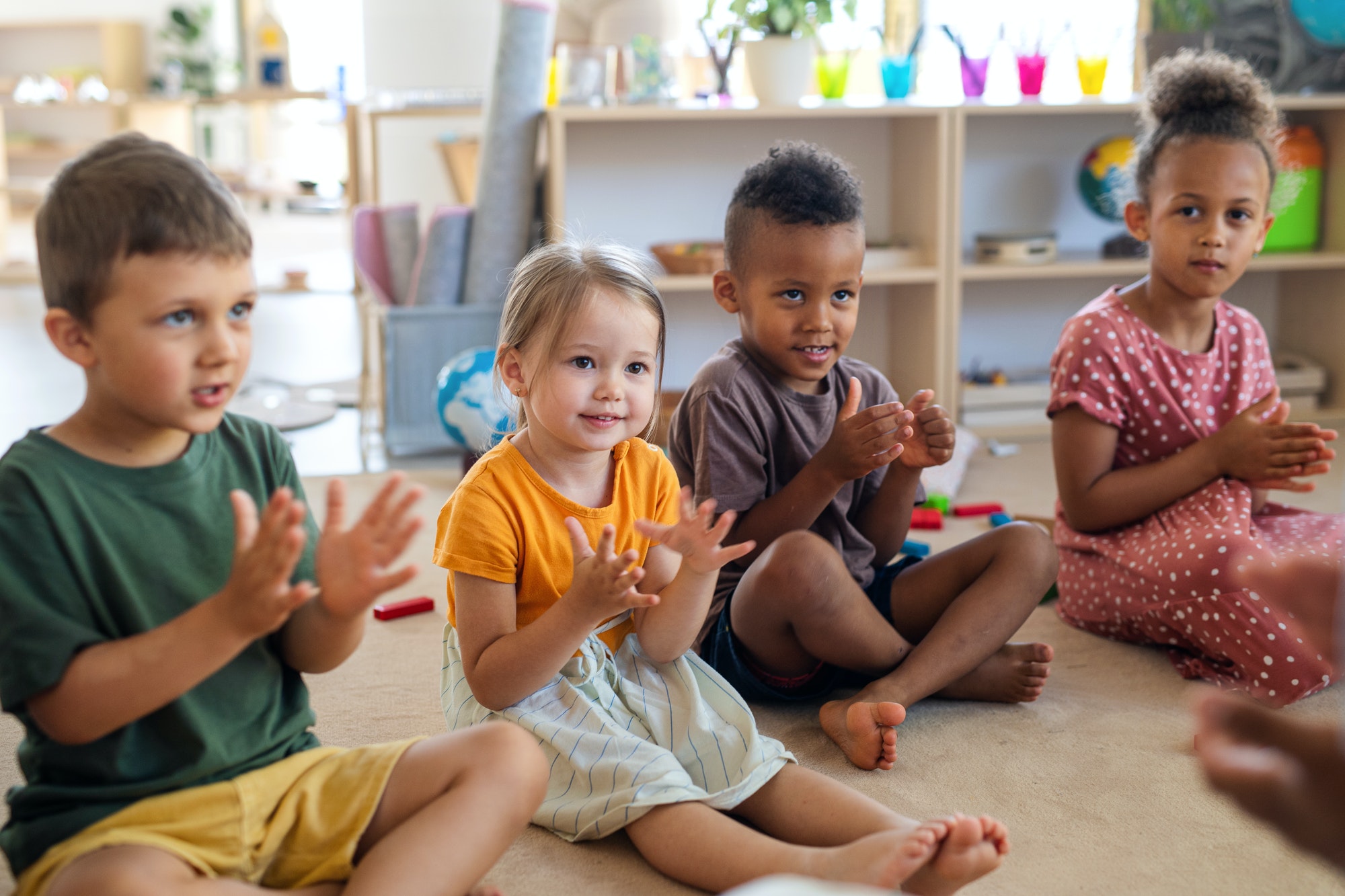 Group of small nursery school children sitting on floor indoors in classroom, clapping