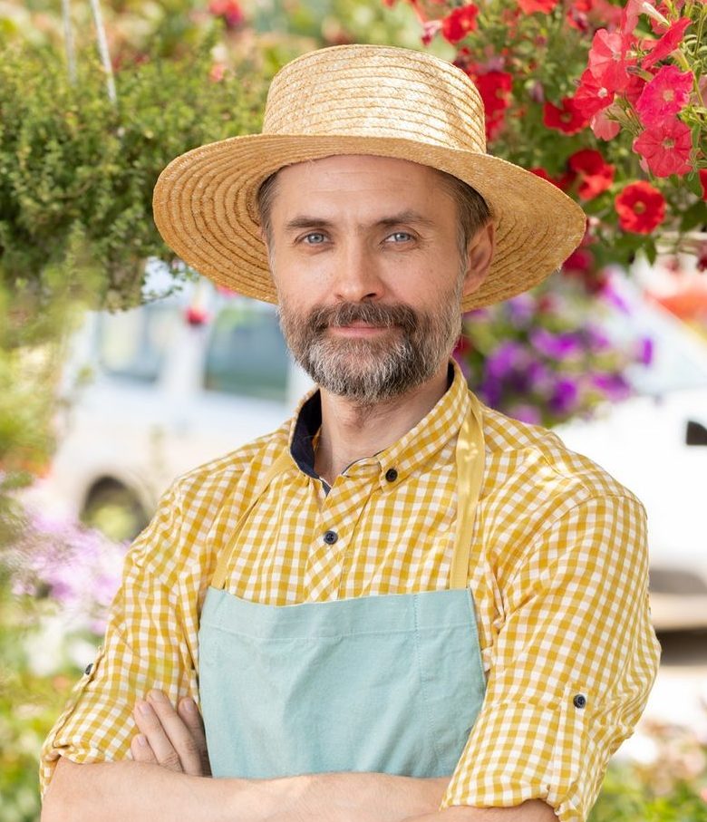 Mature male farmer or gardener in apron and hat standing in greenhouse