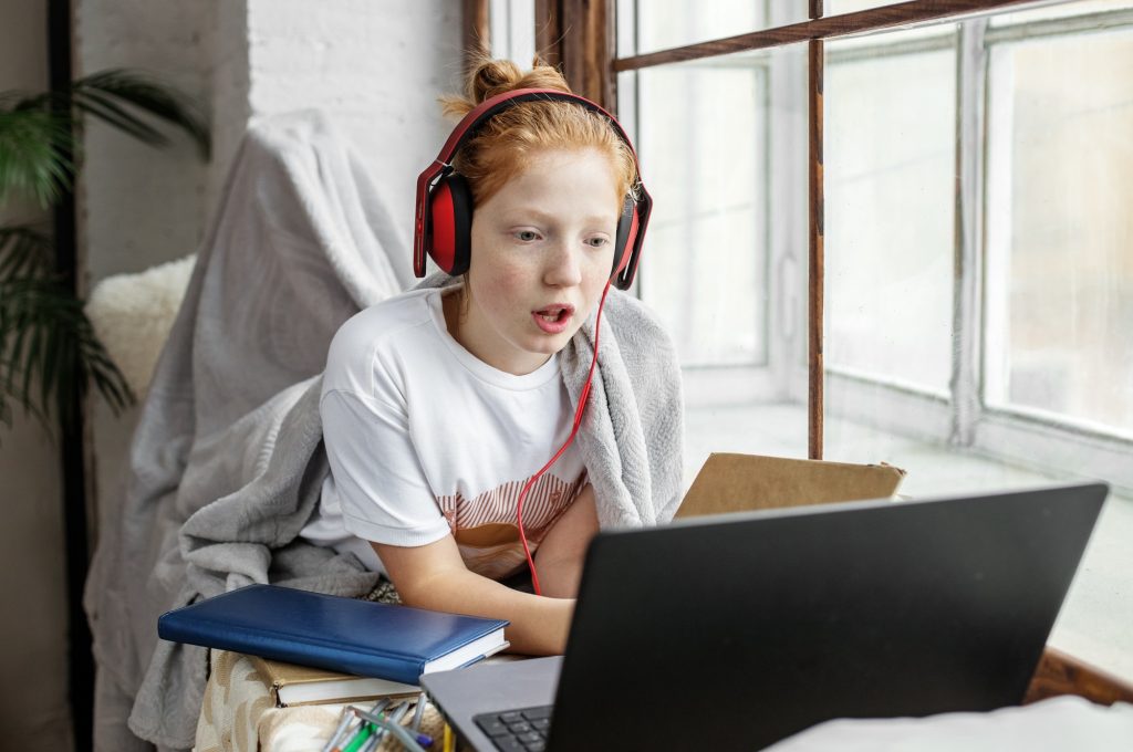 The schoolgirl is studying remotely. Child with headphones and a laptop. Online courses.