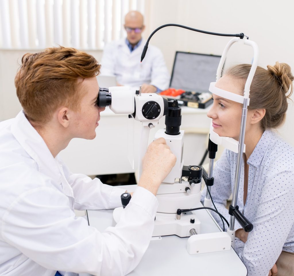 Young optometrist looking through lens of eyesight check-up equipment