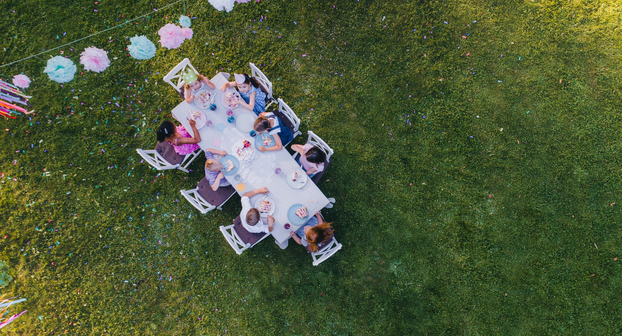 Aerial view of small children sitting at the table outdoors on garden party.