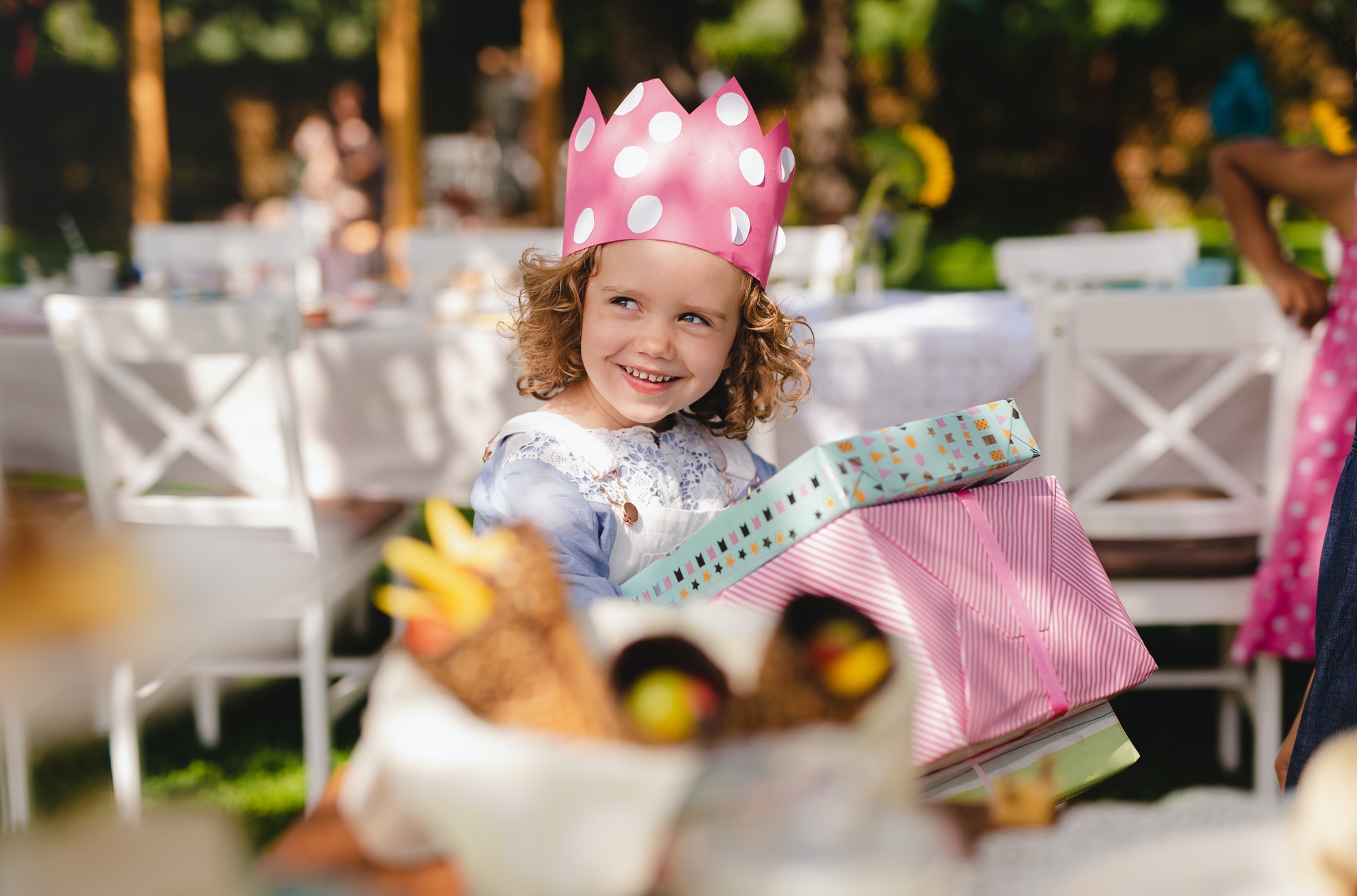 Small girl outdoors in garden in summer, holding presents