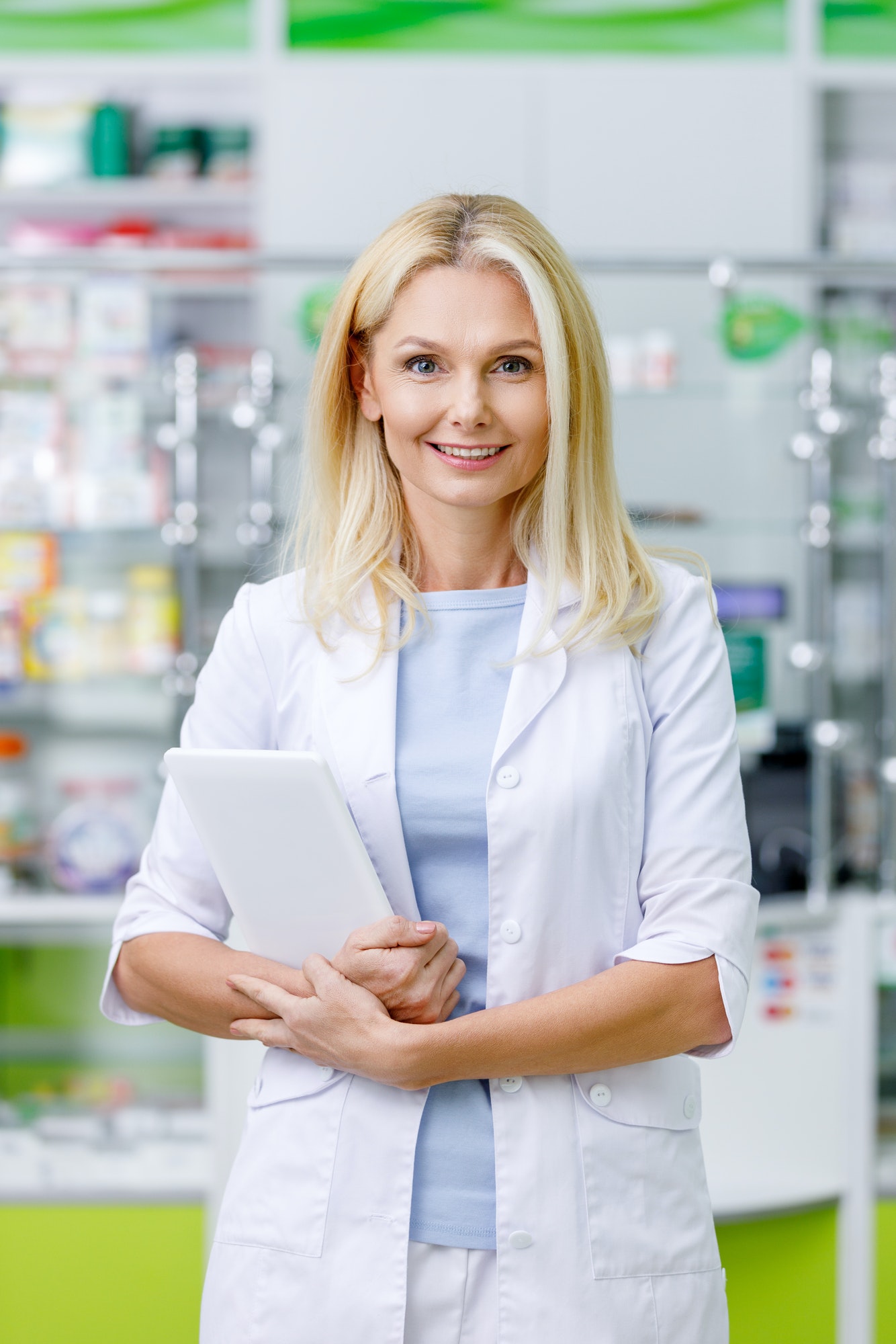 female pharmacist in white coat holding digital tablet and smiling at camera