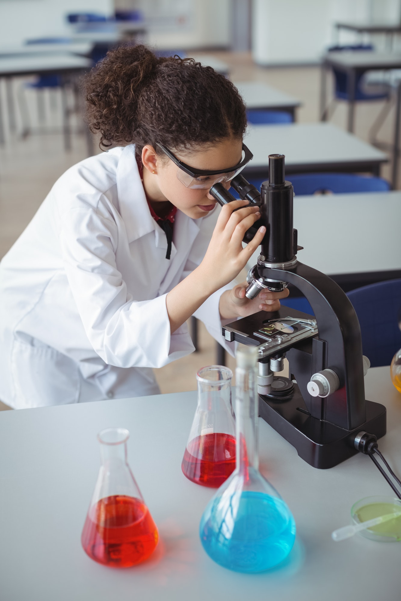 Attentive schoolgirl looking through microscope in laboratory