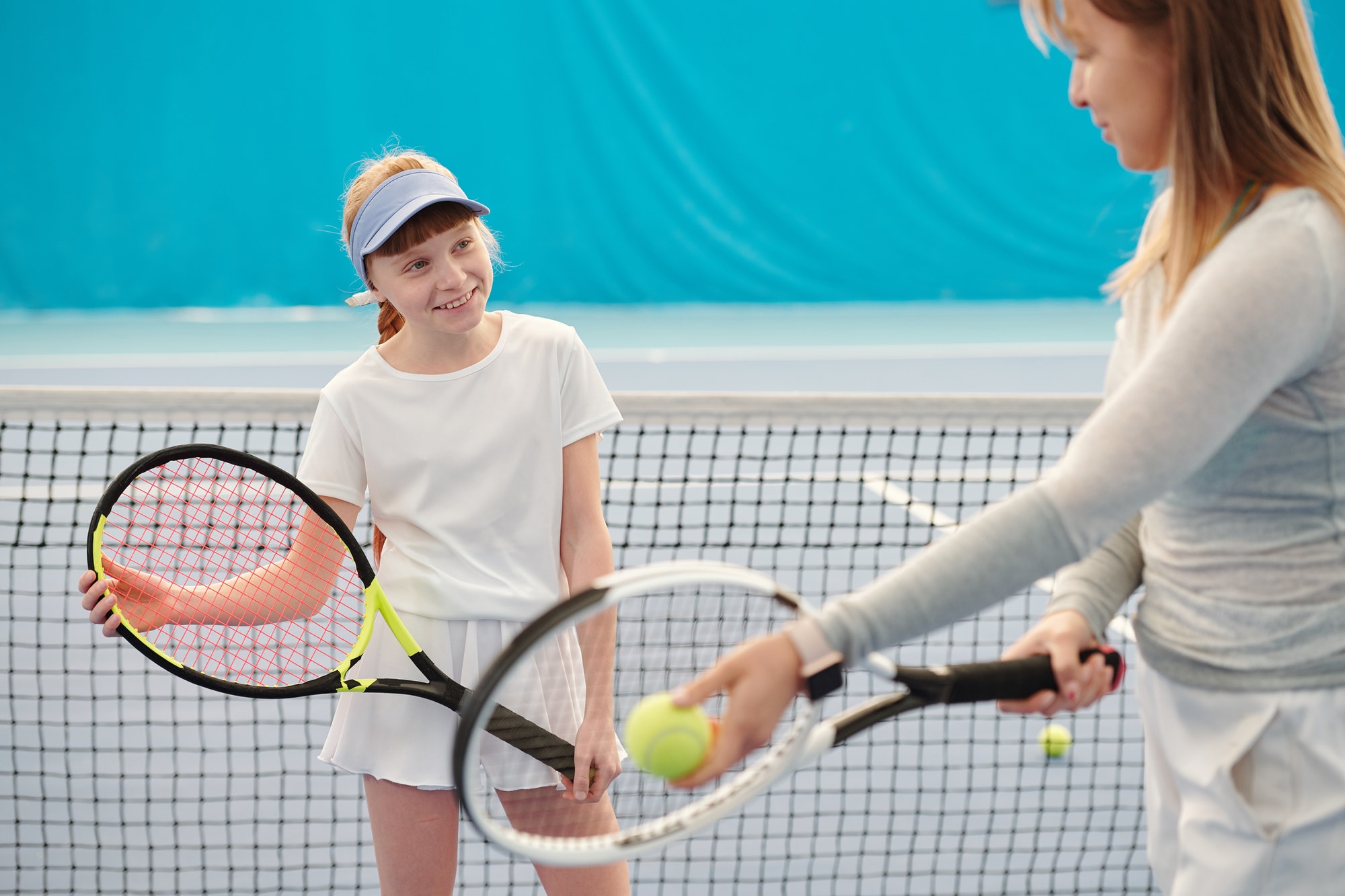 Active girl with tennis racket looking at trainer explaining how to use it