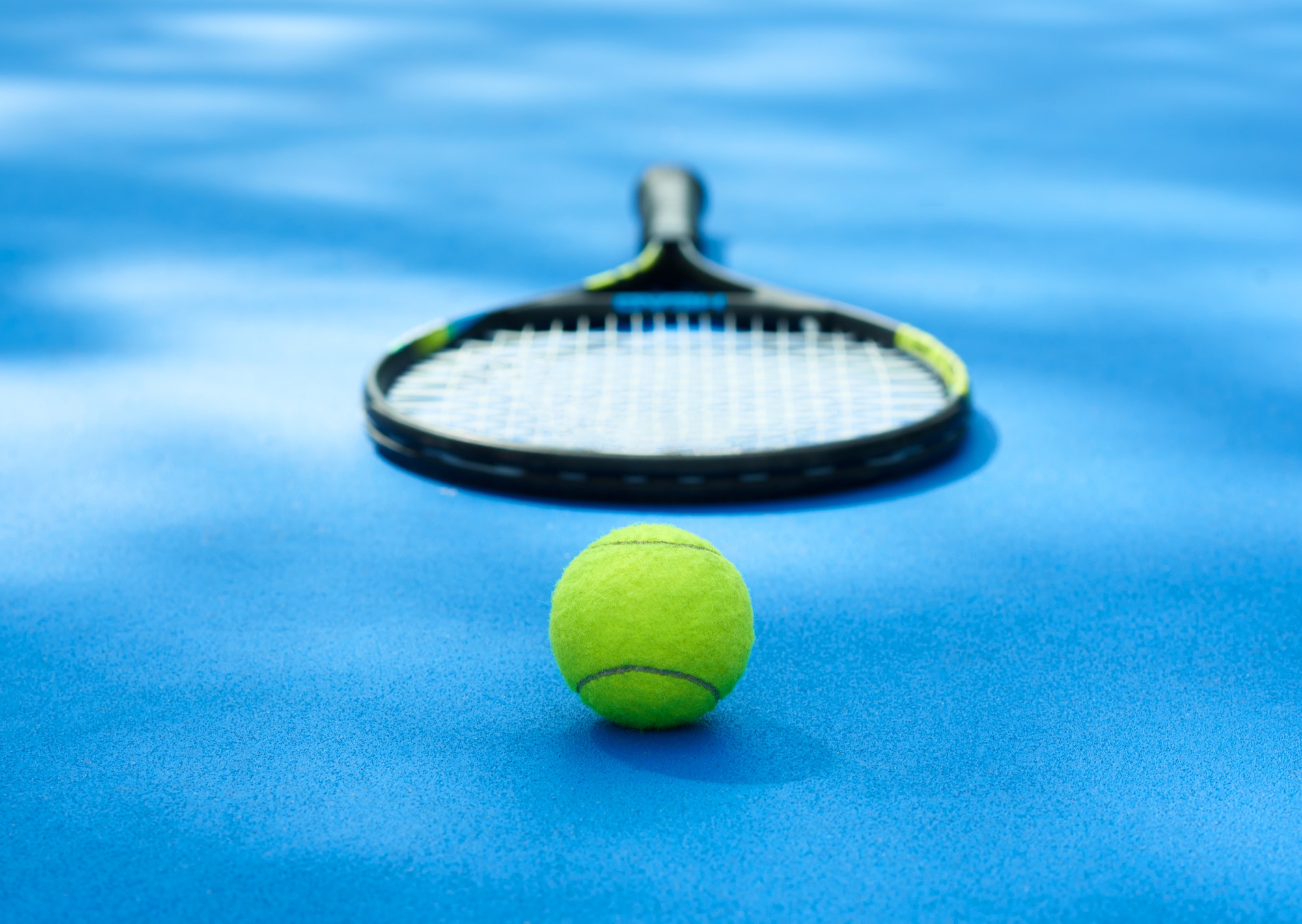 Tennis ball is laying near racket on blue cort carpet