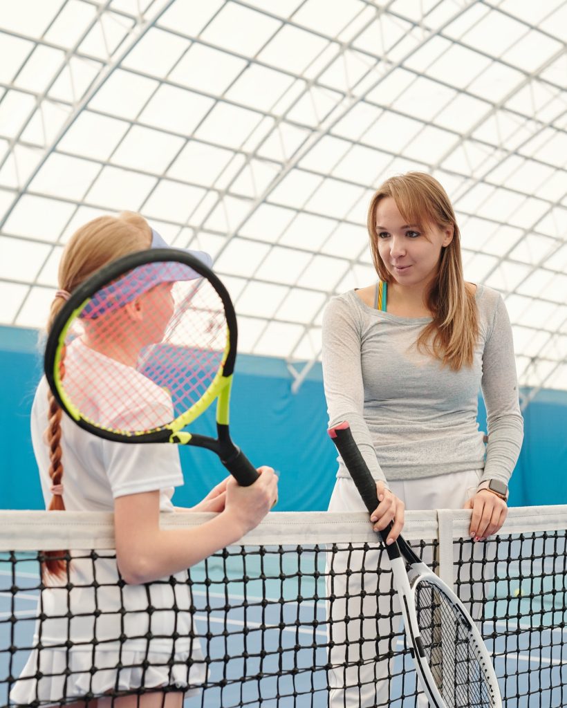 Young female tennis trainer in activewear and cute girl with tennis rackets