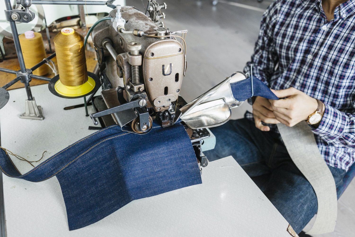 Midsection of tailor sewing jeans in factory