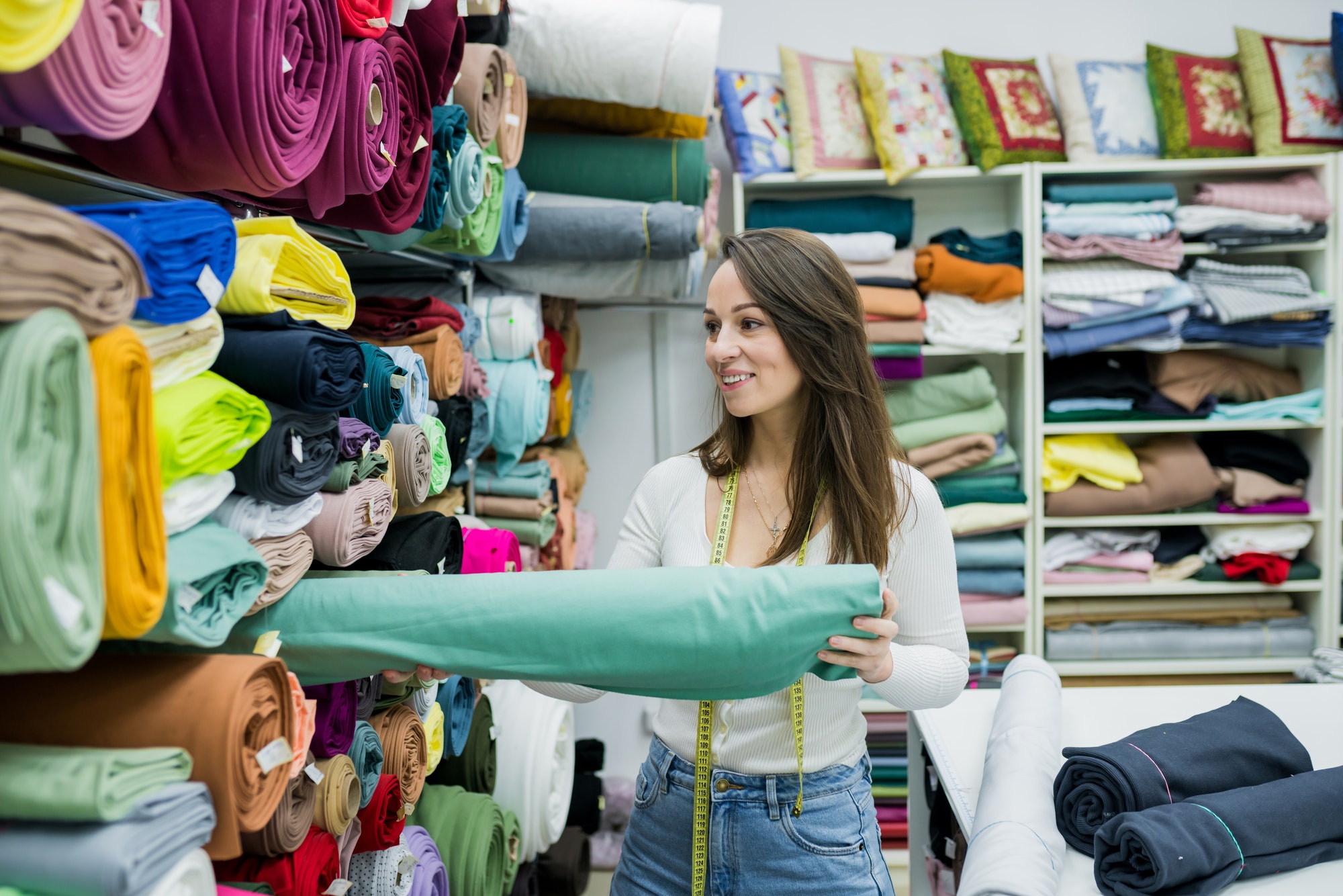 Woman seller standing near work place in fabric store. Owner textile shop holding tissue.