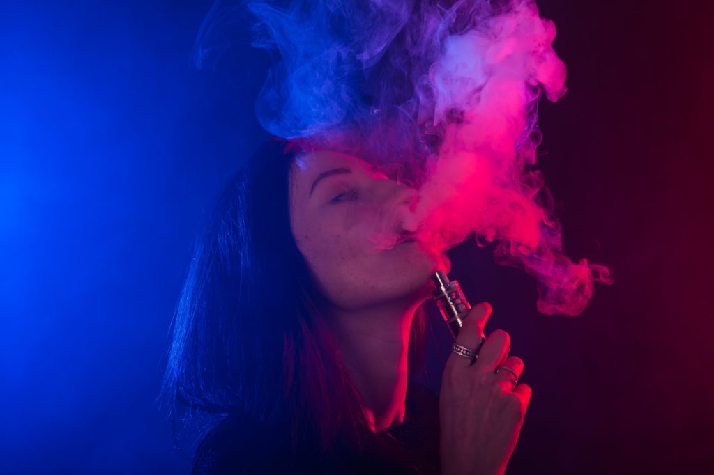 Young woman smoking vape or e-cigarette in neon light