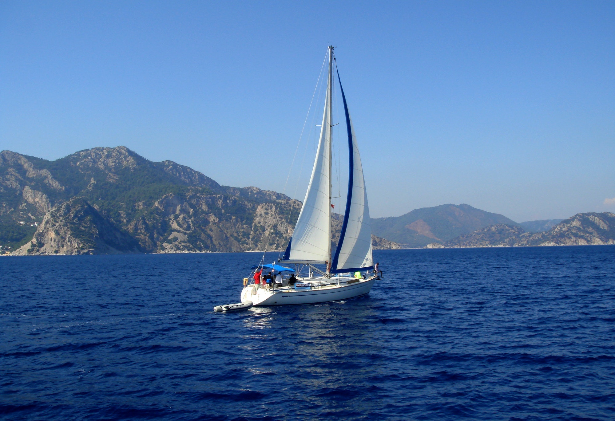 Yacht with white sail sailing on a calm sea on a background of mountains.