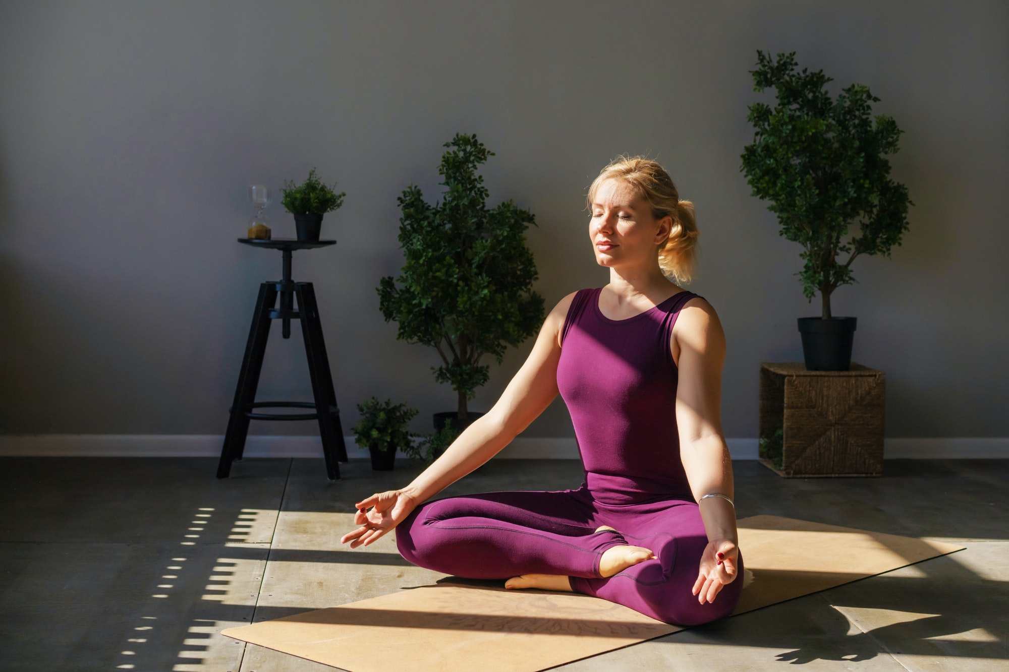 Attractive woman in sportswear sitting on the floor in lotus position meditation at home.